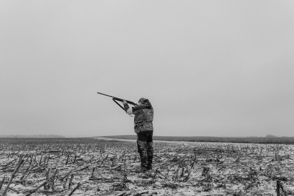 Black and white image of a hunter aiming a rifle in a desolate, snowy field.